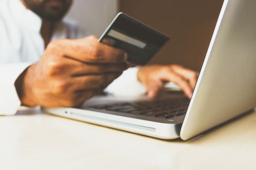 A person holding a credit or debit card in front of a laptop